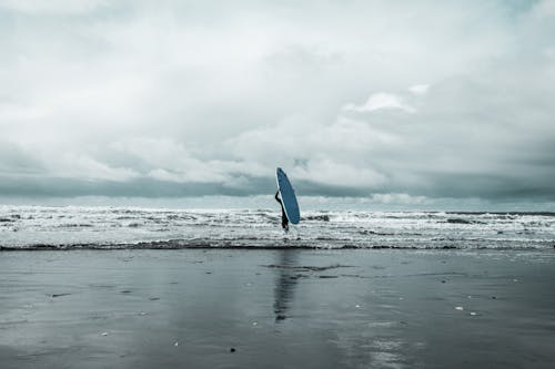 Person Holding Surfboard on Beach
