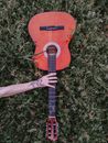 Crop tattooed musician with acoustic guitar on grass
