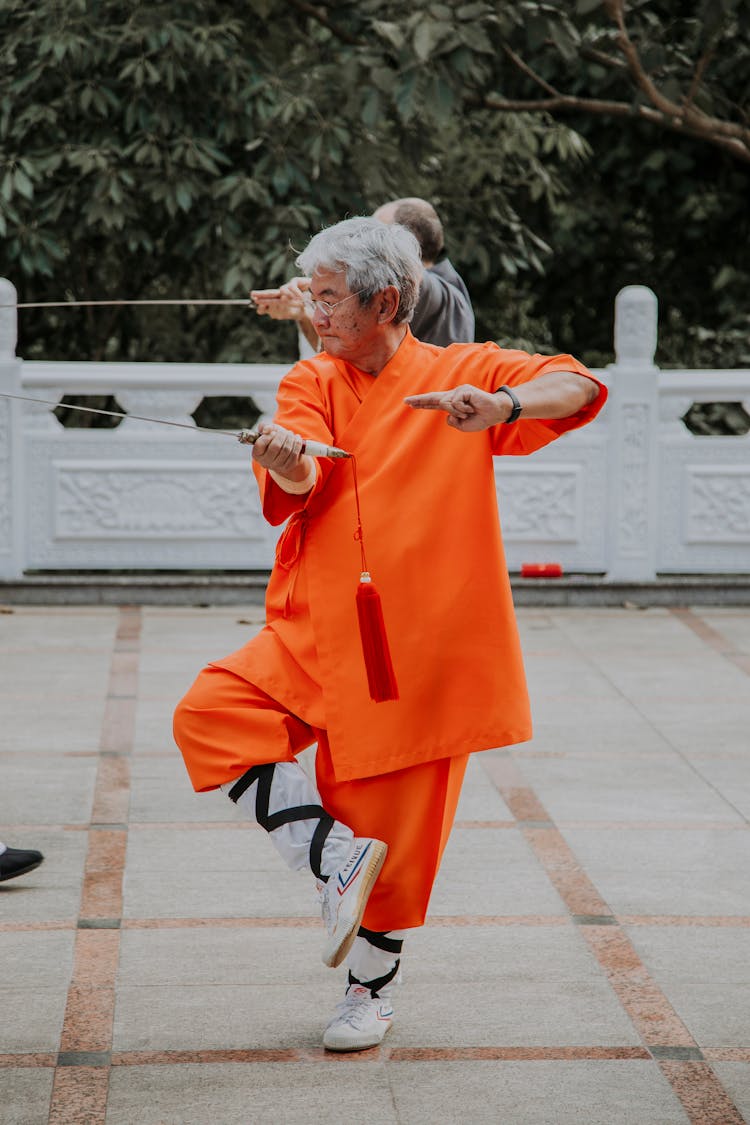 Elderly Asian Man In Bright Outfit Practicing Oriental Martial Art