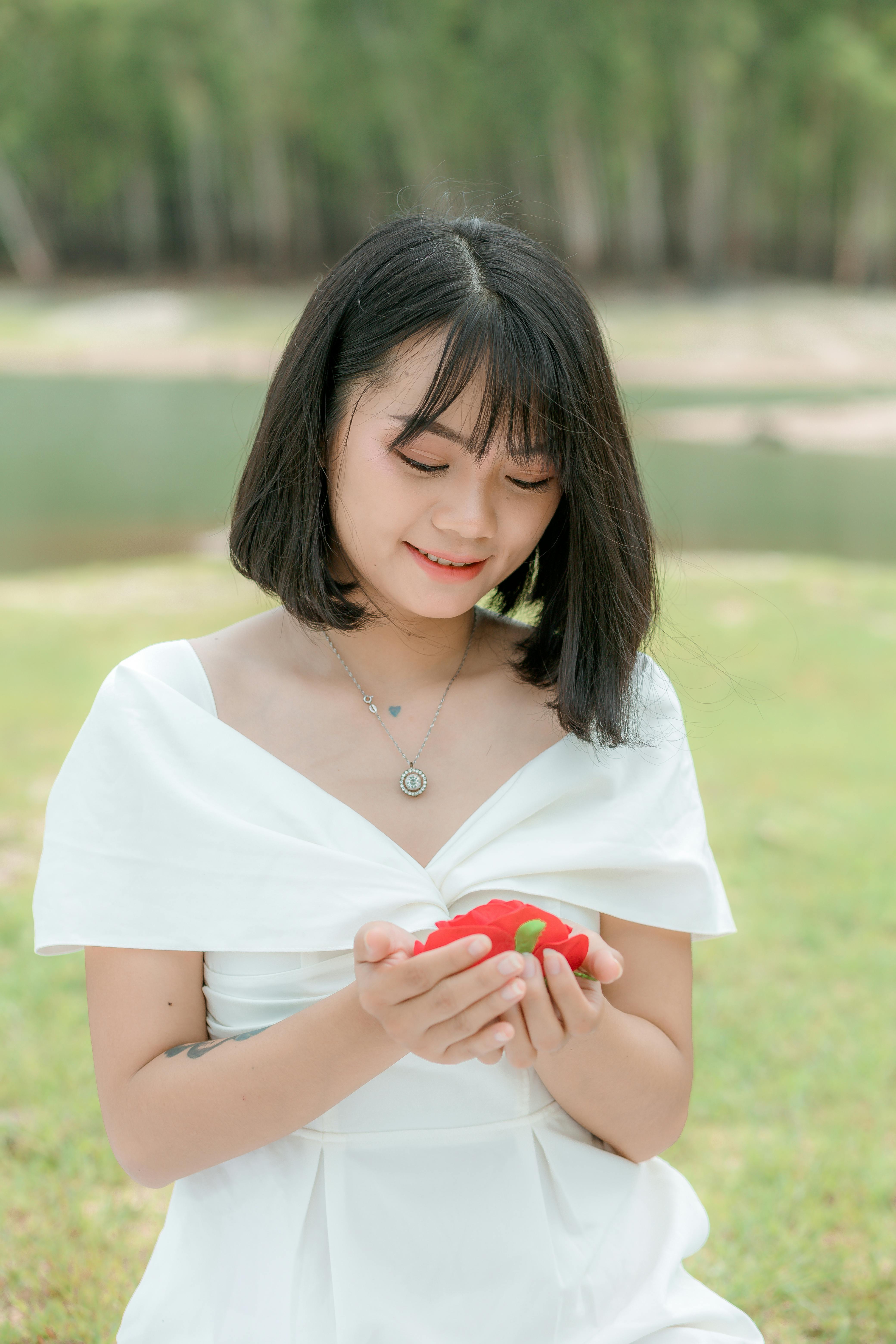 一位开朗的少数族裔女性身着优雅的白色连衣裙，手里拿着红色的花蕾