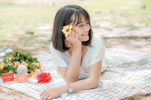Free Cheerful ethnic lady with bright flower resting on meadow Stock Photo