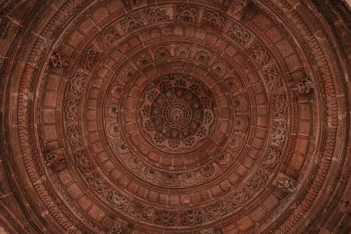 From below of aged stone circle shaped ceiling with geometric decor and small statues in temple