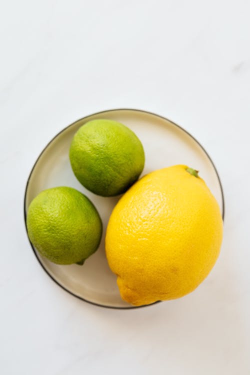 Top view of big whole lemon and limes placed on metal plate on white surface