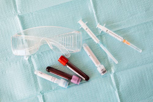 Free Top view of empty and full of blood vials and plastic syringes and eyeglasses  placed on medical diaper Stock Photo