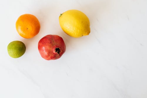 From above of various colors ripe lime and tangerine and pomegranate and lemon placed on white table