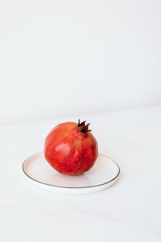 Whole ripe pomegranate placed on white metal plate on white table surface against gray background