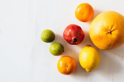 Free Top view closeup of whole ripe limes and tangerines and lemon and pomegranate and grapefruit arranged randomly on white surface Stock Photo