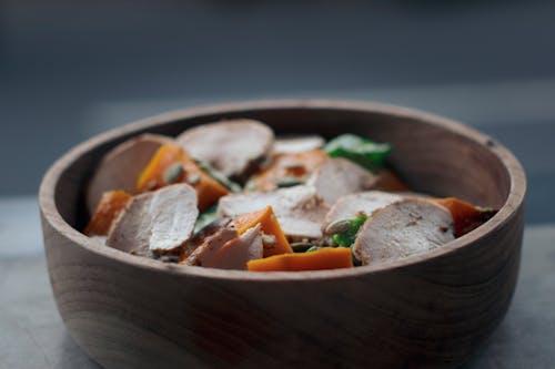 From above of appetizing salad with thin chicken slices and vegetables in wooden bowl on table