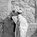 一名男子身穿传统犹太服装，在历史悠久的石墙前祈祷