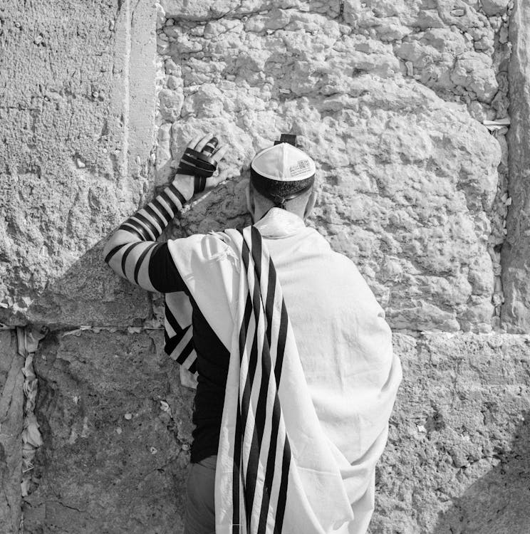 Anonymous Jewish man in traditional wear praying near old wall