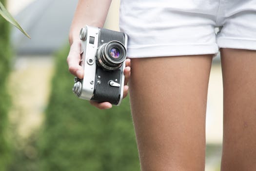 A young woman holds a vintage camera outdoors, wearing white shorts. Stylish and classic photo.