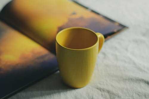 From above of colorful ceramic cup near open book with illustration on crumpled fabric