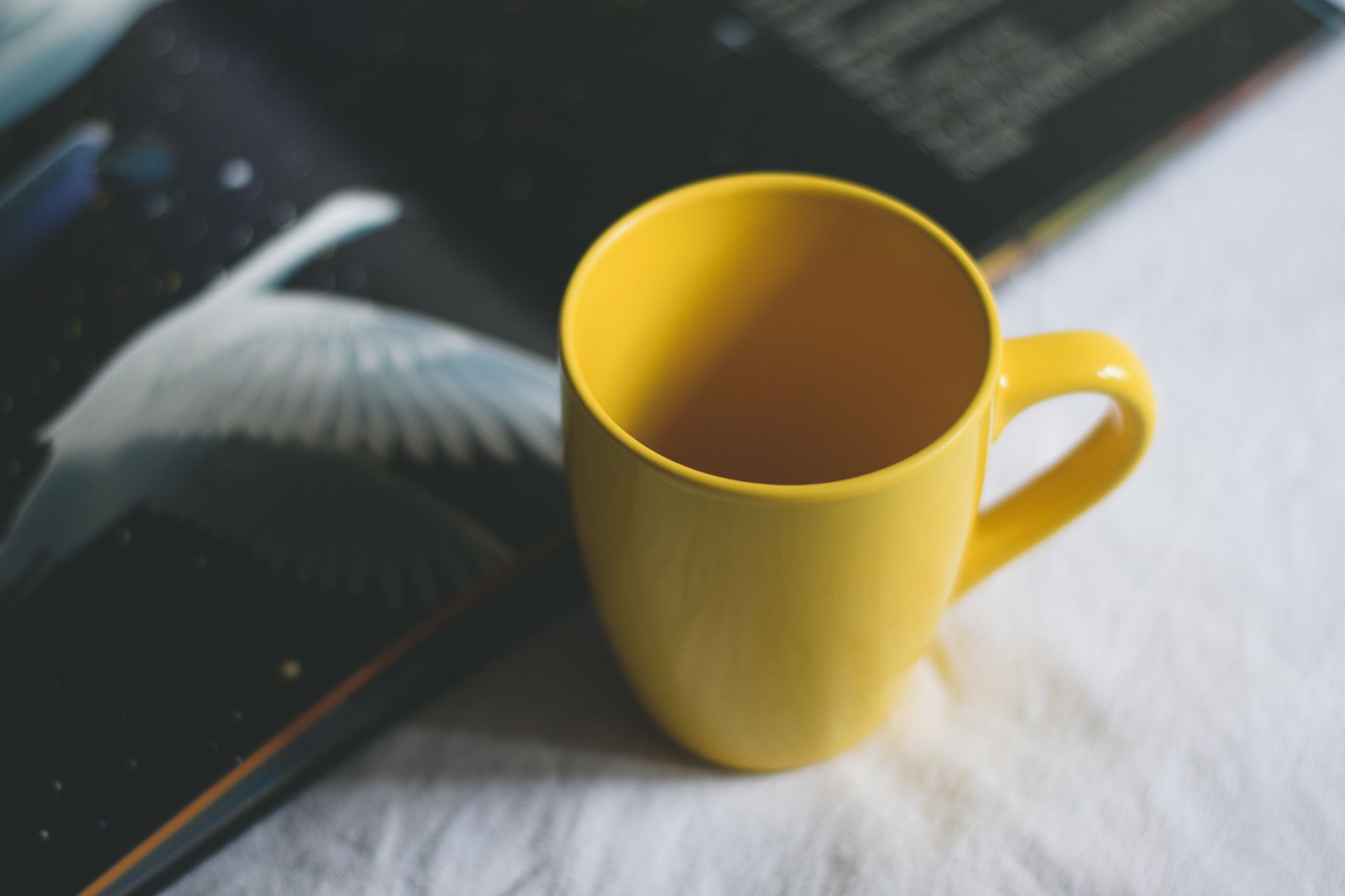 A cozy setting featuring a vibrant yellow mug beside an open book with a bird illustration on a white fabric surface.