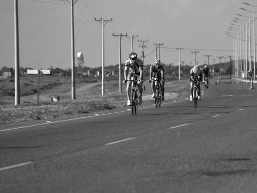 Monochrome Shot of Cyclists Riding their Bicycles on a Concrete Road