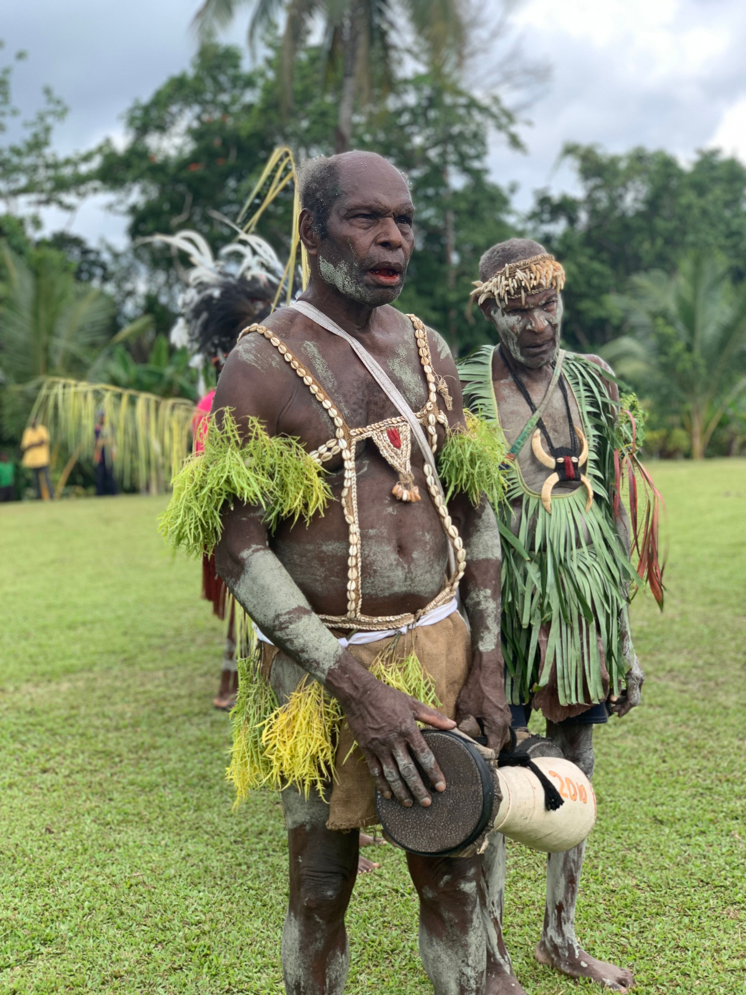 Ethnic partners in traditional wear with percussion musical instrument standing on green meadow and looking away