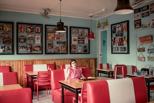 A woman in a pink dress sitting in a retro-style diner in the Philippines.