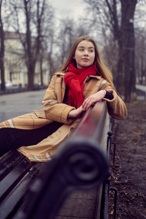 Free Woman in cozy plaid coat and red scarf sits on park bench during winter day. Stock Photo
