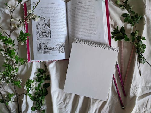 Close-Up Shot of Book and Sketchbook on White Textile