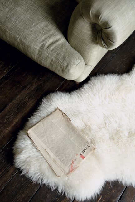 An old newspaper placed on a fur rug next to a sofa in a cozy indoor setting with wooden floors.