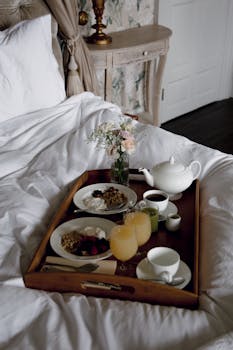 Elegant breakfast in bed setup with tea and flowers in a cozy bedroom setting.
