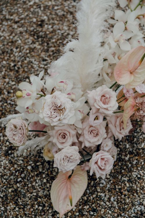 Free A delicate arrangement of pink and white flowers, including roses and lilies, with feathers on a gravel background. Stock Photo