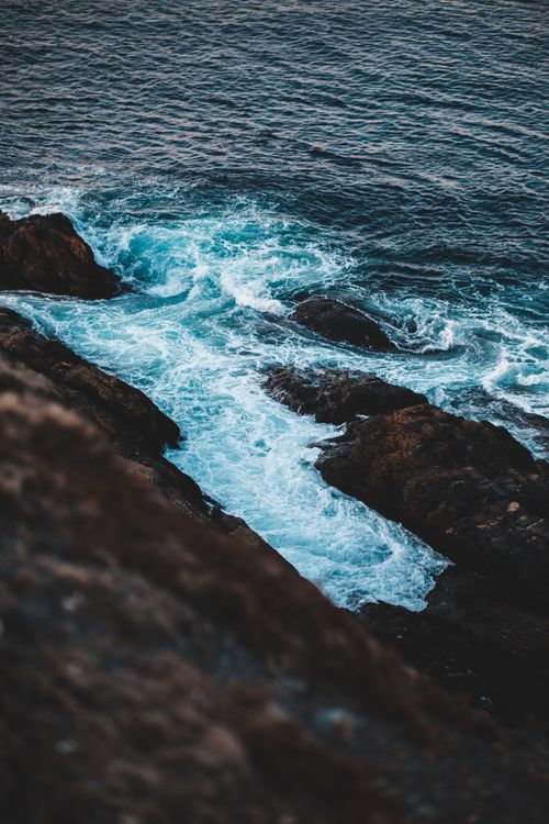 Free From above scenery view of wavy sea with rippled water forming foam near rough mount with uneven surface in afternoon Stock Photo