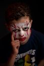 From above of concentrated adolescent with deep gaze and fearful greasepaint on face with red lips looking at camera while standing with finger up on black background at night