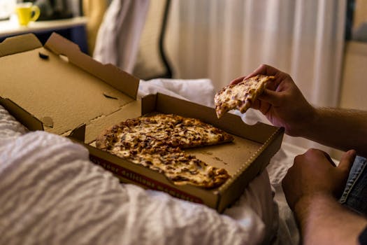A person enjoying a tasty pizza slice in a cozy bedroom setting.