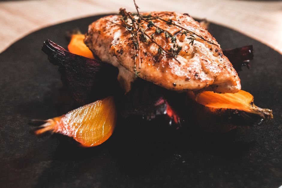 Halved red and golden roasted beets with charred, wrinkled skins on a baking sheet, one beet peeled to show the deep magenta flesh underneath.