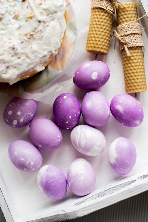 Top view of purple colored Easter eggs and delicious panetonne with rolled beeswax candles placed on white background