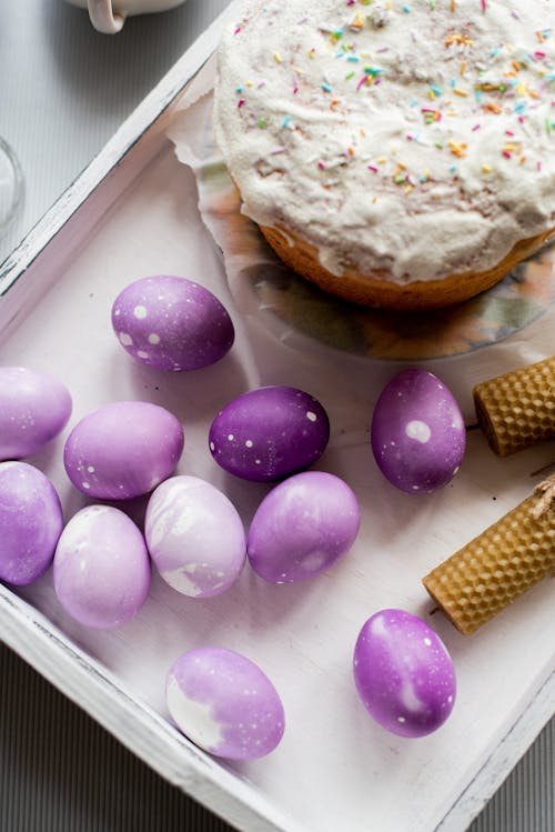 From above of tasty Easter cake and eggs of purple color with rolled beeswax candles placed in white container