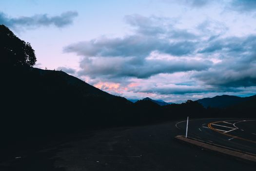 Curvy asphalt roadway on slope of mountain ridge against sky with dark evening clouds