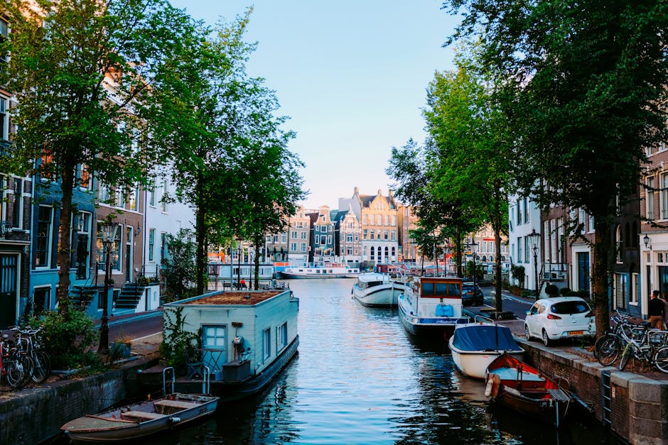 Peaceful scenery of Amsterdam streets with typical houses against channel with moored boats on clear sunny day