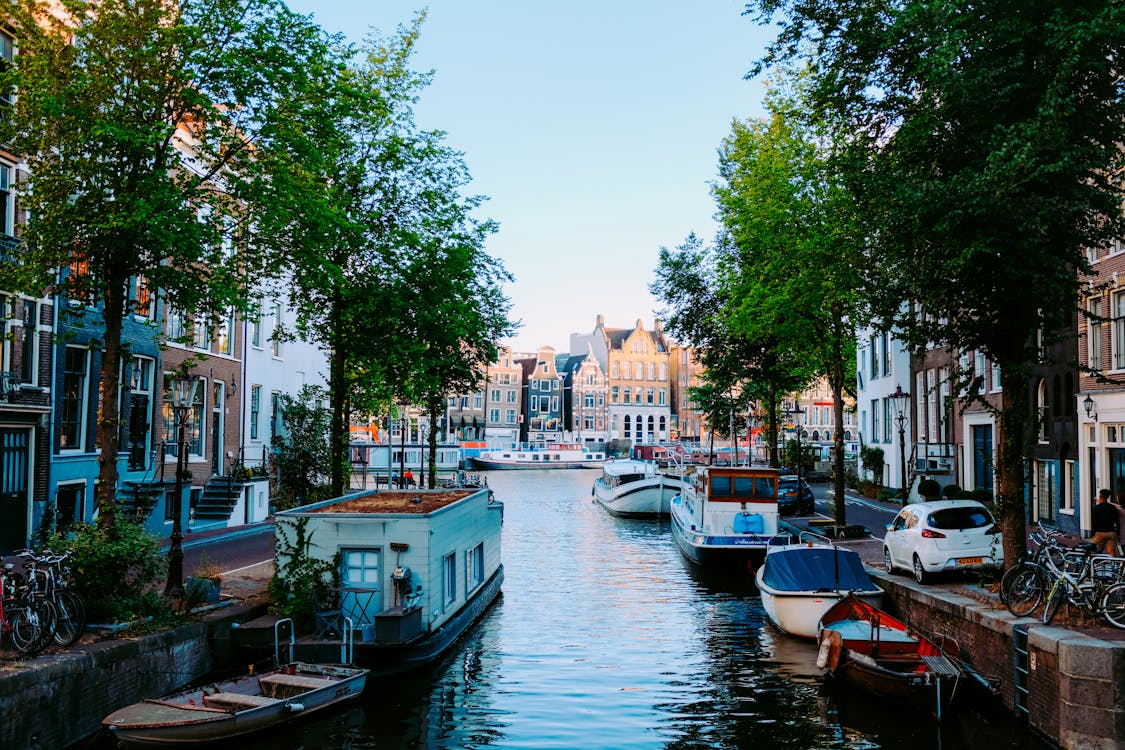 Free Peaceful scenery of Amsterdam streets with typical houses against channel with moored boats on clear sunny day Stock Photo