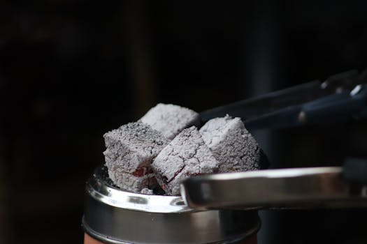 Closeup metal tongs putting hot coal on hookah kaloud bowl in dark room