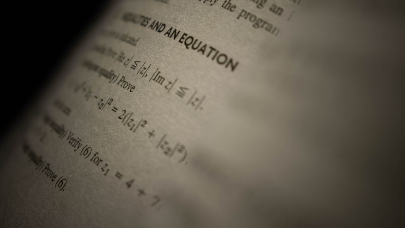 Selective focus on a mathematics textbook page with complex equations and text.