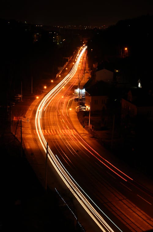 Drone view long exposure of illuminated asphalt roadway running through suburb with moving vehicles at dark night