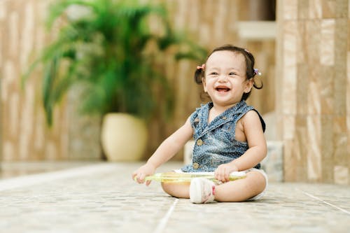 Photo of an Adorable Kid Laughing while Sitting on the Floor