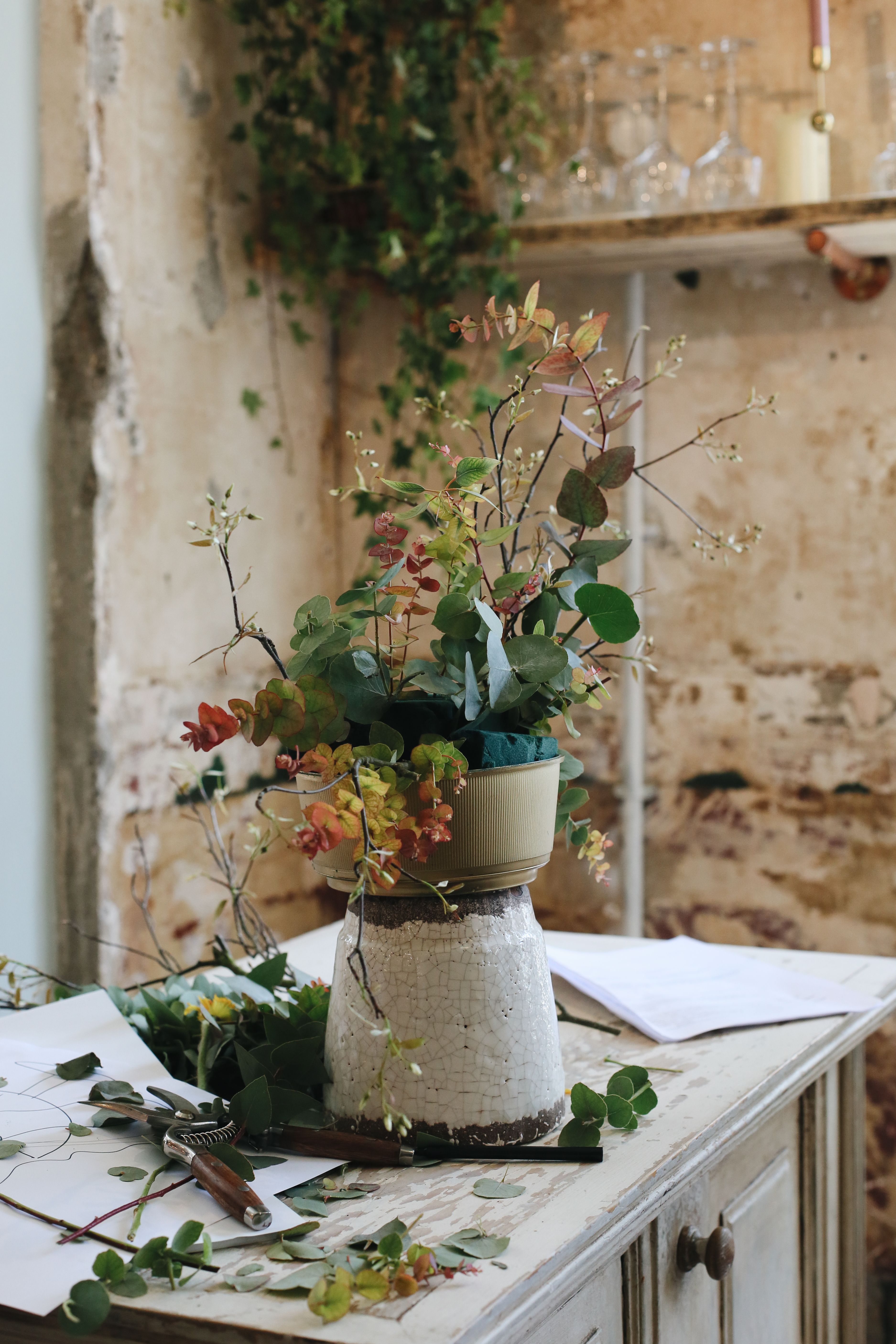 Artistic floral arrangement with greenery on a rustic table against a textured wall, perfect for decor inspiration.