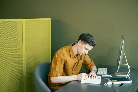 一个穿着棕色衬衫的男人，在现代化办公室的整洁办公桌前，用笔记本素描