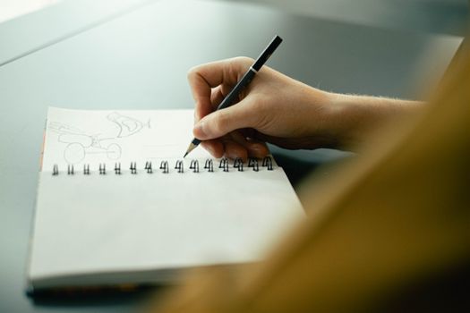 Hand sketching in a notebook with a pencil, focusing on creativity and planning.
