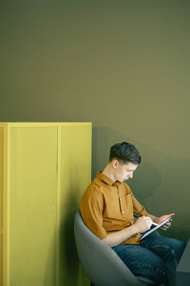 Man Sitting On A Chair And Writing On A Tablet