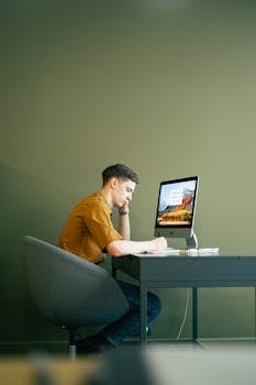 Man focused on work at home office desk with computer, displaying concentration and modern workspace.