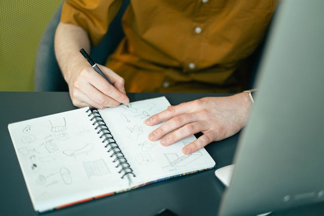 Hands sketching interface ideas into a notebook at a desk — photo by Ivan S on Pexels