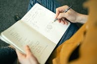 Person Holding Pen and Writing on a Notebook