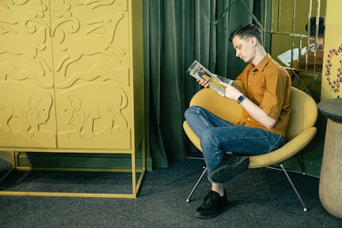 Man Sitting on a Chair and Reading a Magazine