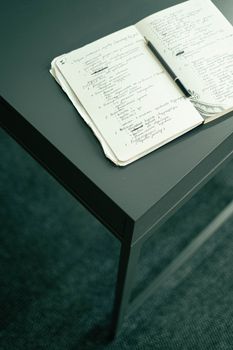 Open notebook on a dark desk with handwritten notes and pencil in a minimalist setup.