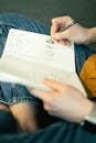 Person Holding a Pen and Writing on a Notebook