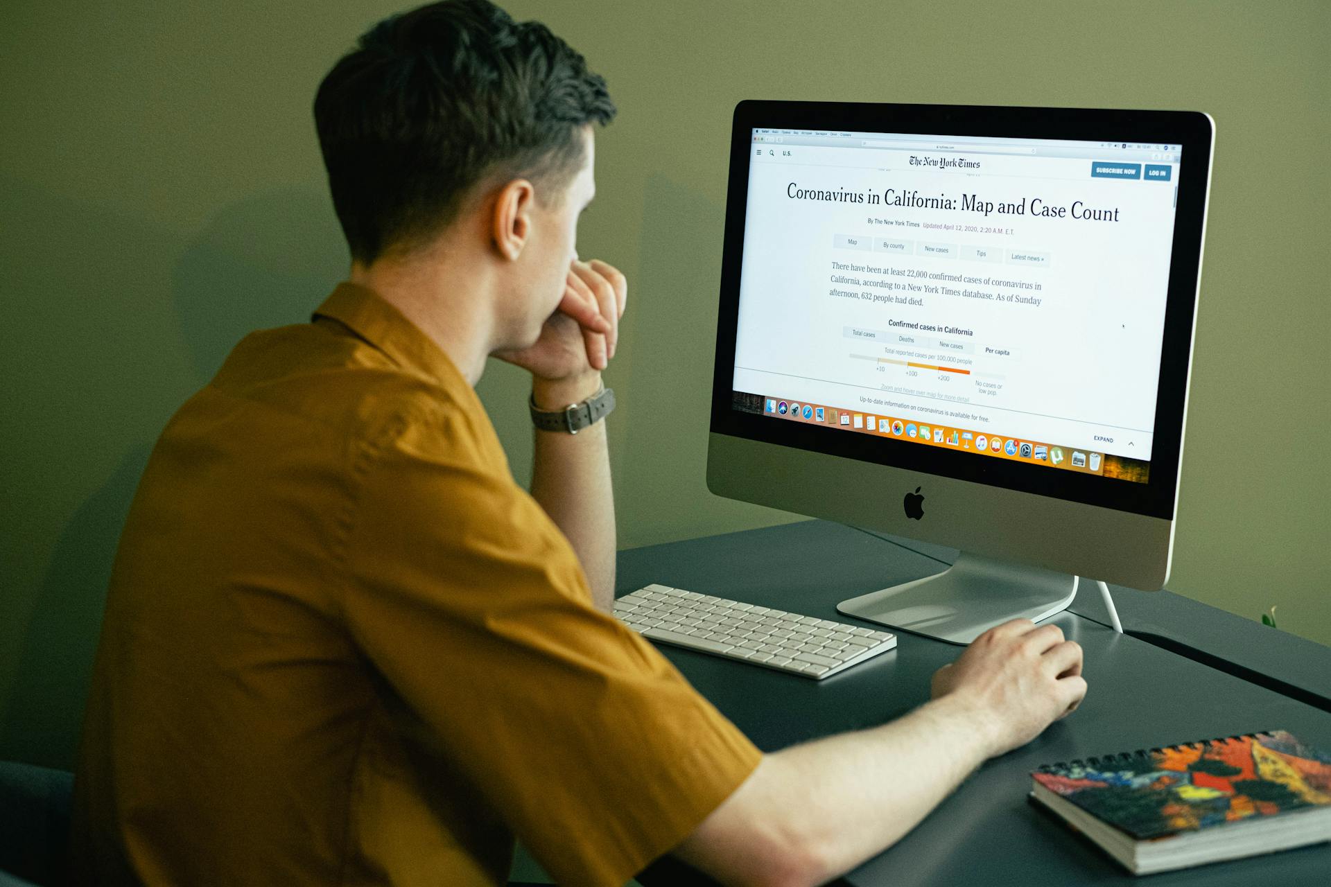 Man in a home office reading coronavirus map and case update on computer screen.