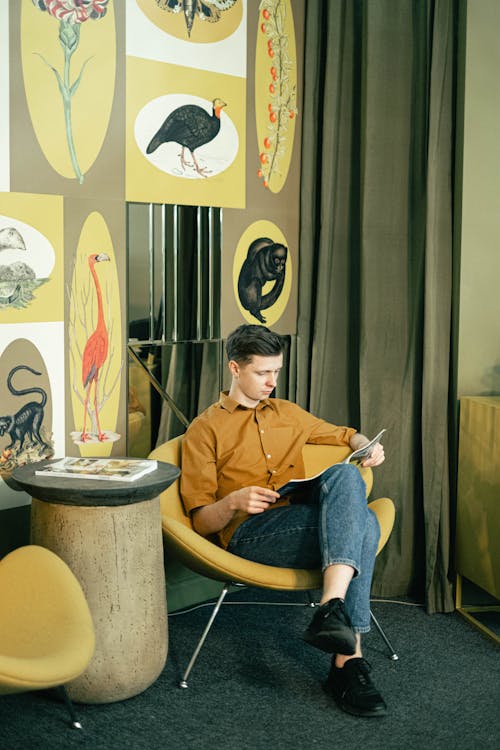 Free Man Sitting on a Chair and Reading a Magazine Stock Photo
